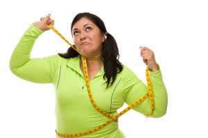 Attractive Frustrated Hispanic Woman Tied Up With Tape Measure Against a White Background.